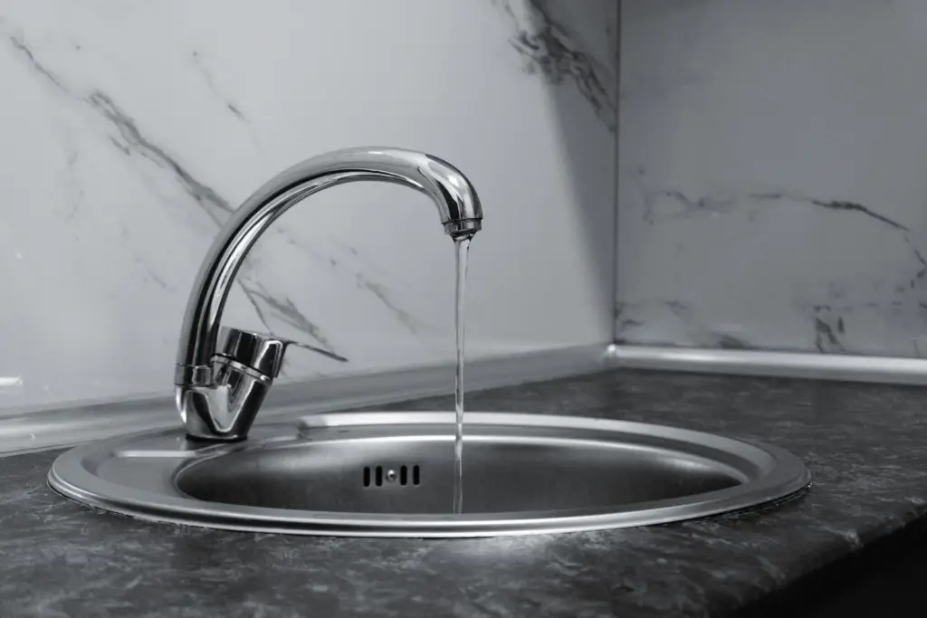 Chrome kitchen faucet with running water over a marble countertop