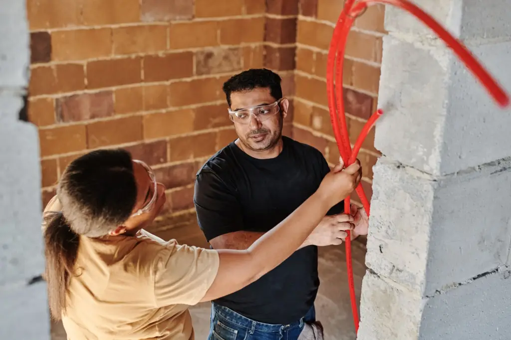 Two plumbers working together to fit pipe through a wall